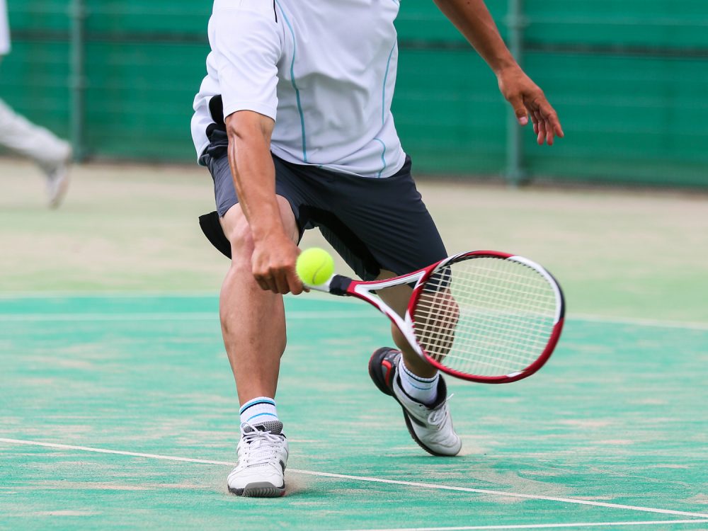 テニスでバックハンドをする男性